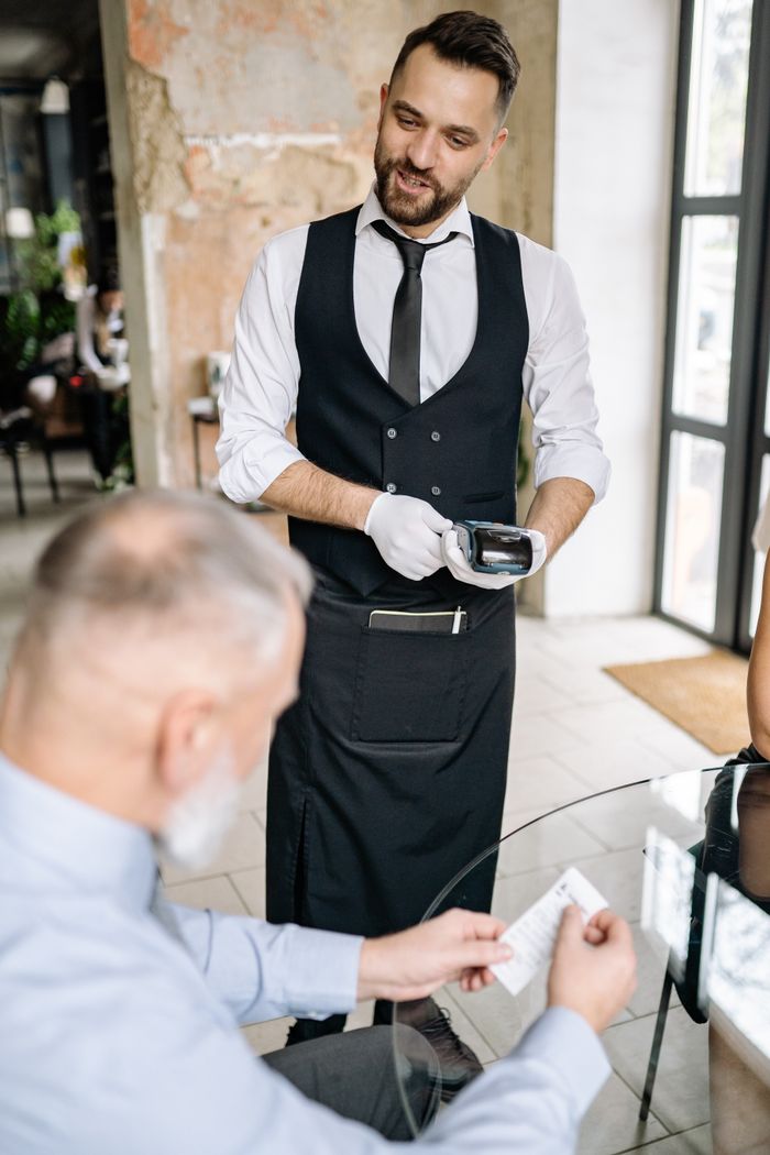 A waiter processes payment using a terminal while a customer reviews the bill, showcasing excellent service.